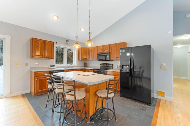 kitchen featuring a breakfast bar, a center island, light countertops, brown cabinetry, and black appliances