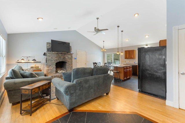 living area featuring vaulted ceiling, ceiling fan with notable chandelier, a fireplace, and hardwood / wood-style flooring