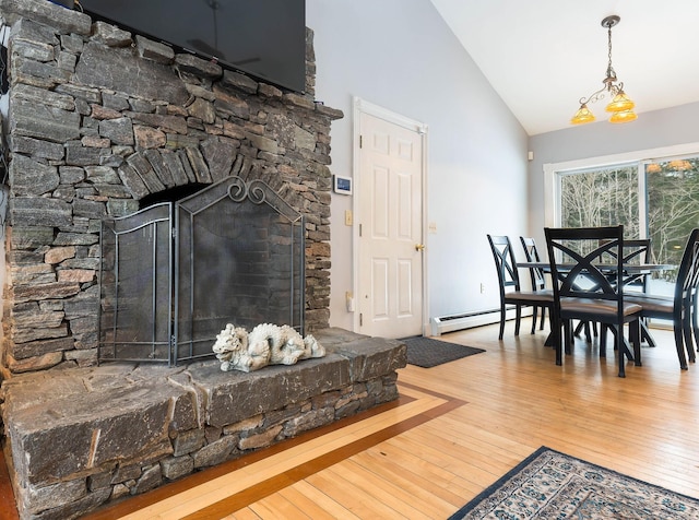 dining area with high vaulted ceiling, a stone fireplace, baseboard heating, and wood finished floors