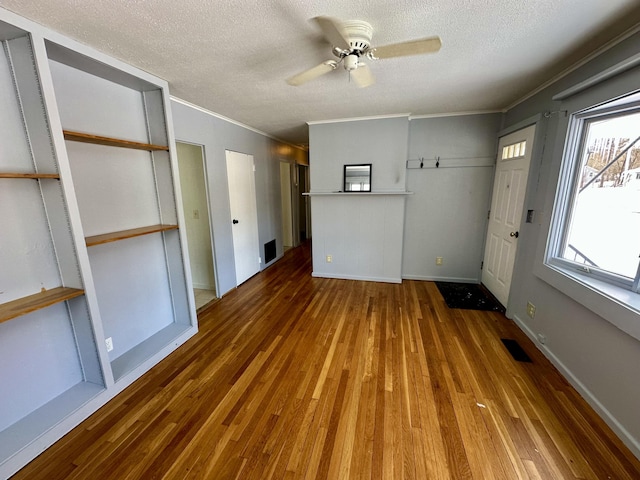 unfurnished living room featuring wood-type flooring, visible vents, ornamental molding, a ceiling fan, and a textured ceiling