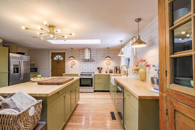 kitchen with green cabinetry, appliances with stainless steel finishes, wall chimney exhaust hood, and butcher block counters