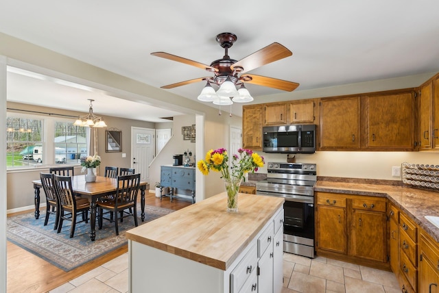 kitchen featuring appliances with stainless steel finishes, hanging light fixtures, brown cabinets, ceiling fan with notable chandelier, and wood counters