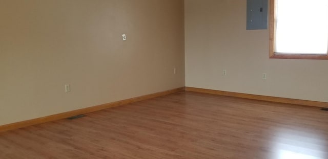 empty room with wood finished floors, electric panel, and baseboards