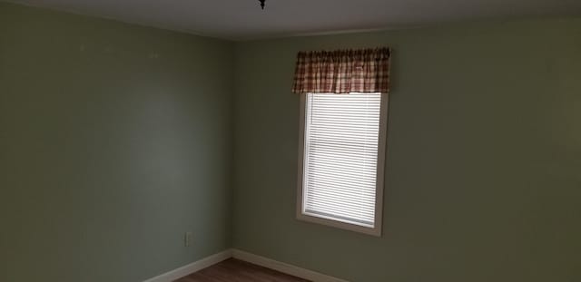 spare room with baseboards and dark wood-type flooring