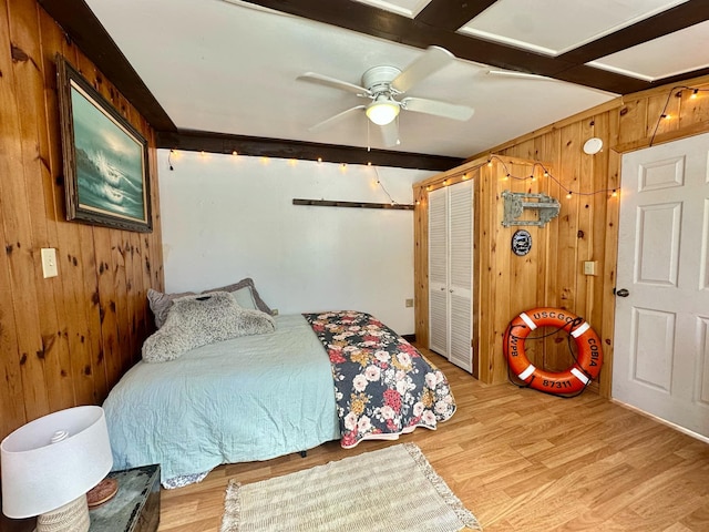 bedroom featuring beamed ceiling, wood finished floors, a ceiling fan, and wooden walls