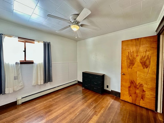 empty room with a baseboard heating unit, visible vents, wood finished floors, and a ceiling fan