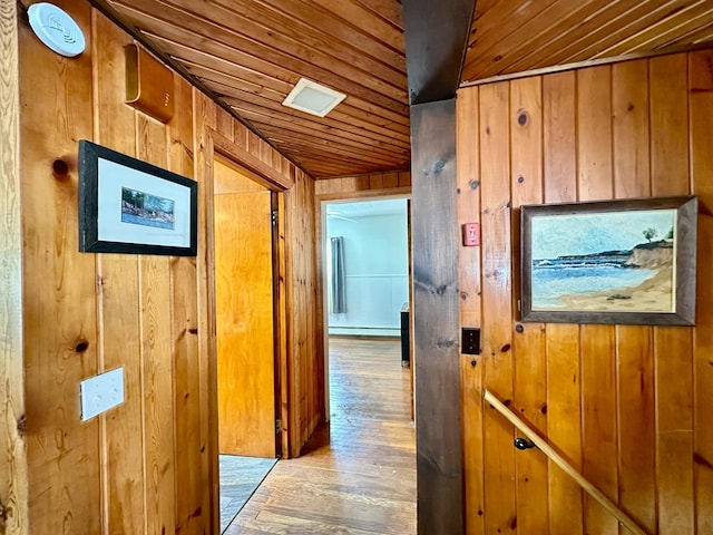 hallway with wooden ceiling, wooden walls, baseboard heating, and wood finished floors