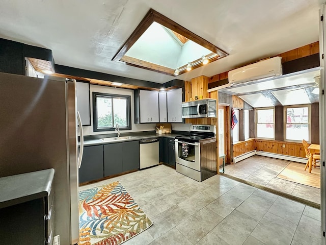 kitchen with a skylight, stainless steel appliances, dark countertops, a baseboard heating unit, and a sink