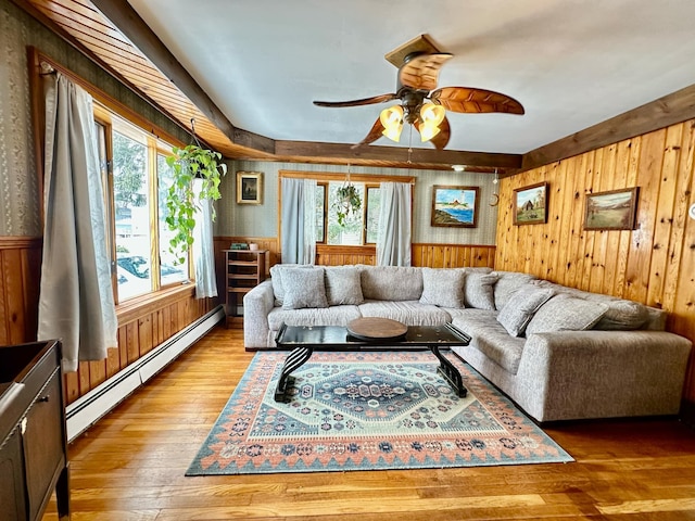 living area featuring a baseboard radiator, wood-type flooring, a ceiling fan, wainscoting, and wood walls