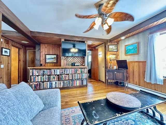 sitting room with wooden walls, a ceiling fan, a wainscoted wall, wood finished floors, and a baseboard heating unit