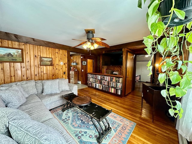 living area featuring ceiling fan, wooden walls, and wood finished floors