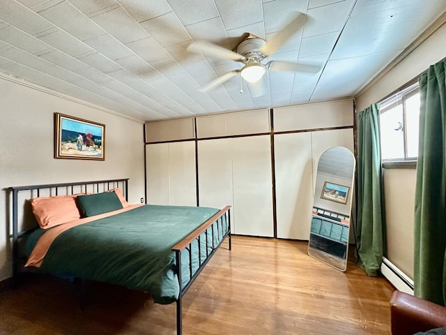 bedroom with ornamental molding, ceiling fan, light wood finished floors, and baseboard heating