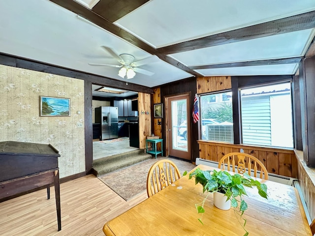 dining room with beam ceiling, baseboard heating, ceiling fan, wooden walls, and wood finished floors