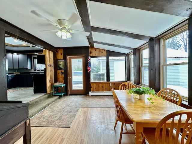 dining space with lofted ceiling with beams, a baseboard radiator, wooden walls, wood finished floors, and a ceiling fan