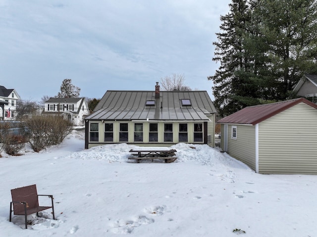 snow covered rear of property with metal roof, a standing seam roof, and a chimney