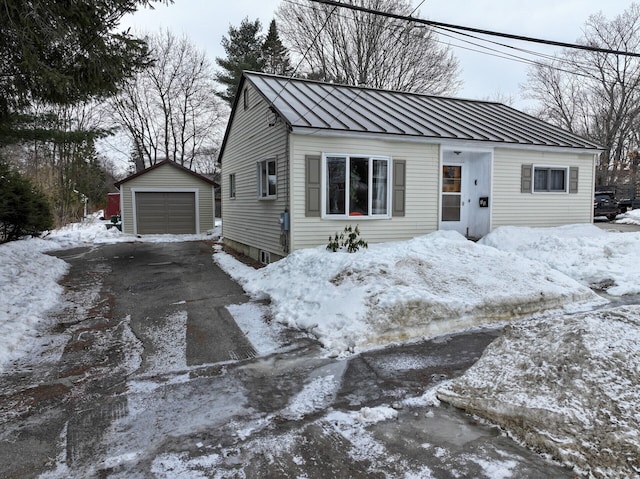 view of front facade featuring an outbuilding, metal roof, a detached garage, driveway, and a standing seam roof