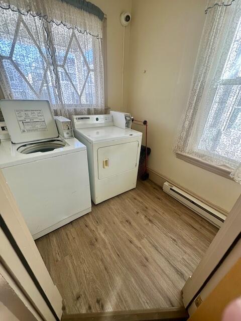 clothes washing area featuring laundry area, baseboard heating, light wood finished floors, and washing machine and clothes dryer