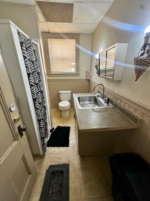 full bathroom featuring a drop ceiling, toilet, vanity, wainscoting, and a shower stall