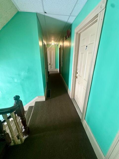 corridor with baseboards, visible vents, and a drop ceiling