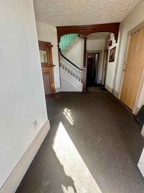 hallway with stairs, a textured ceiling, and baseboards