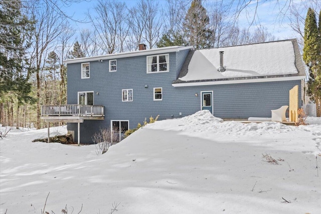 snow covered property with a wooden deck and a chimney