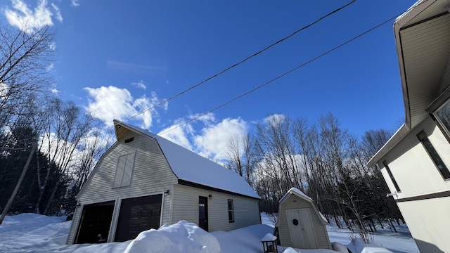 view of snowy exterior featuring a garage, an outbuilding, a barn, and a gambrel roof