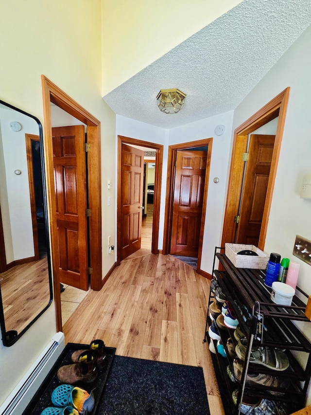 hall featuring a baseboard heating unit, a textured ceiling, baseboards, and light wood-style floors