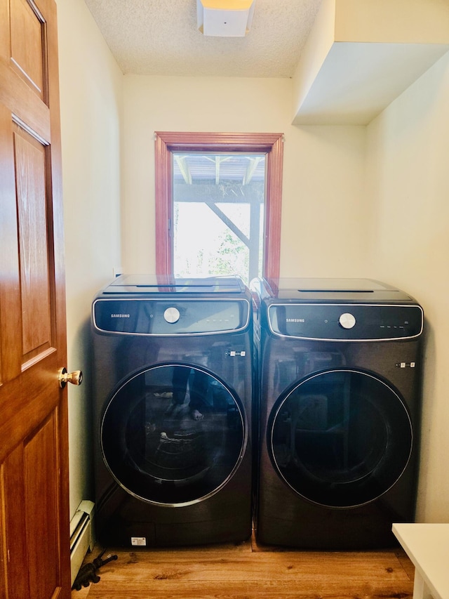 laundry room with a baseboard heating unit, a textured ceiling, wood finished floors, washer and dryer, and laundry area