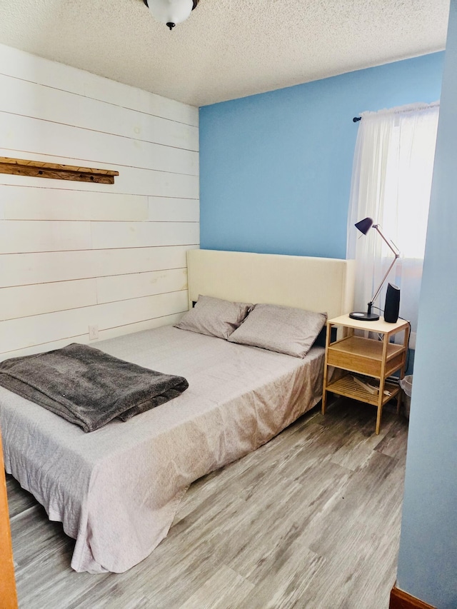 bedroom with wood walls, a textured ceiling, and wood finished floors