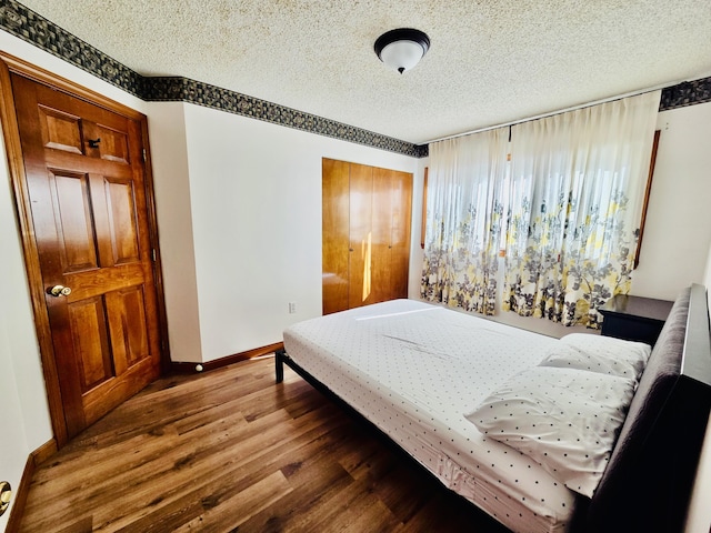 bedroom with a textured ceiling, baseboards, and wood finished floors