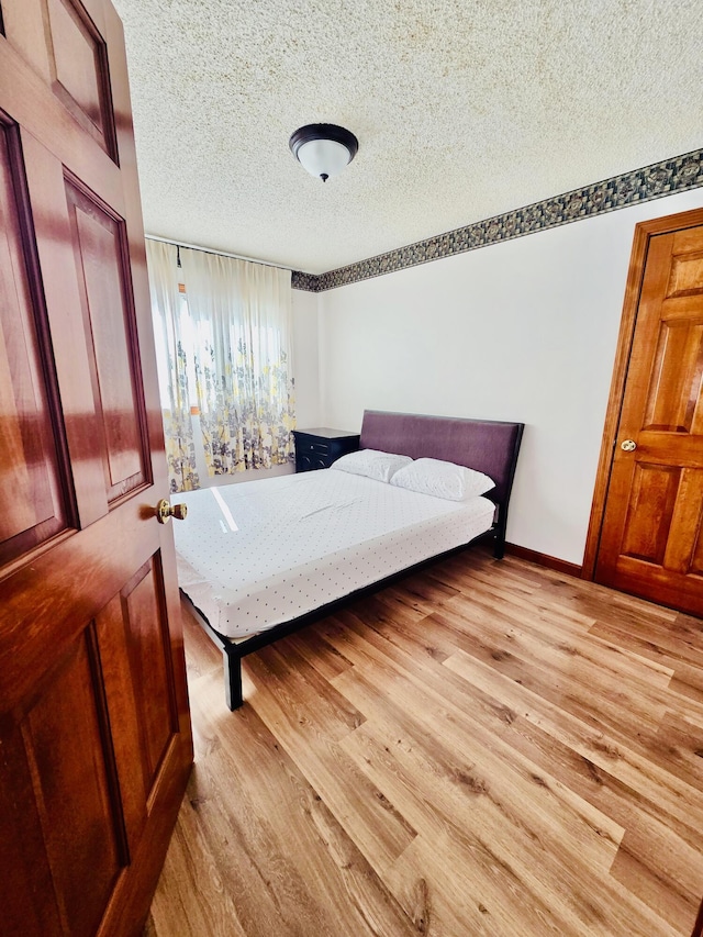 bedroom featuring a textured ceiling, baseboards, and light wood-style floors