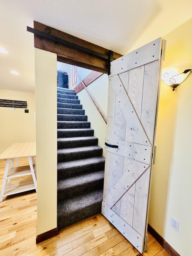 stairway with a barn door, baseboards, wood finished floors, and recessed lighting