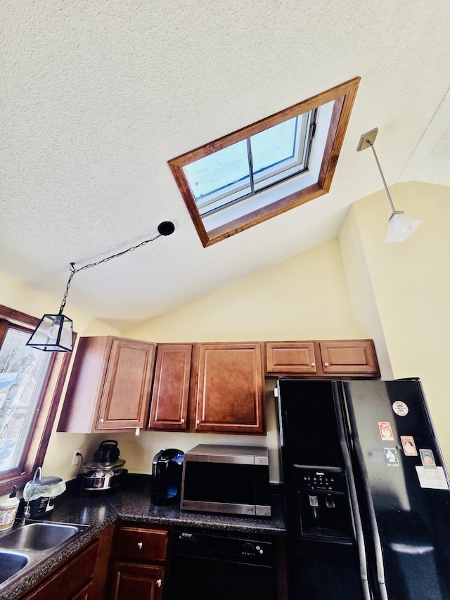 kitchen with a textured ceiling, vaulted ceiling with skylight, a sink, black appliances, and dark countertops