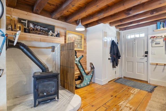 entryway featuring baseboards, wood ceiling, beam ceiling, a wood stove, and hardwood / wood-style flooring