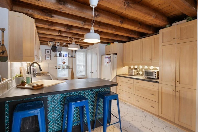 kitchen featuring a sink, beam ceiling, dark countertops, and freestanding refrigerator