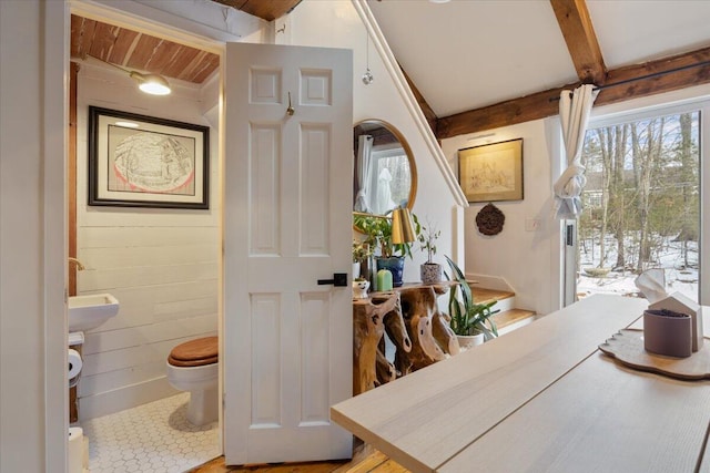 bathroom featuring beam ceiling, toilet, and wood walls