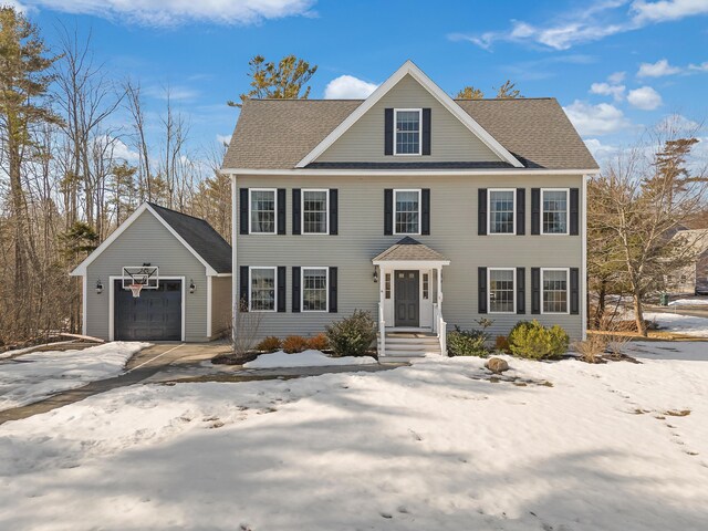 colonial-style house featuring an outbuilding, a shingled roof, and a garage