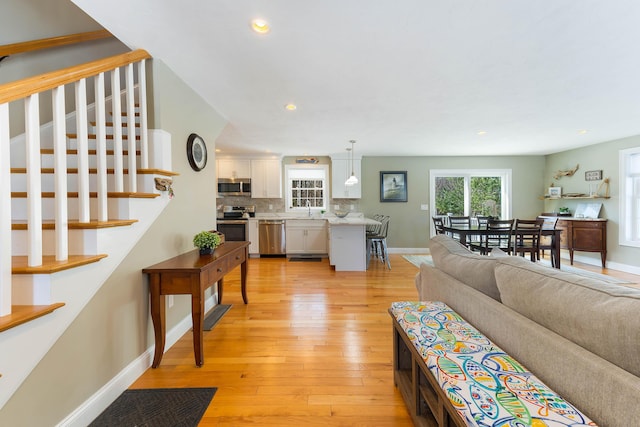 living room featuring stairway, recessed lighting, baseboards, and light wood-style floors