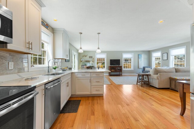 kitchen with light wood finished floors, open floor plan, a peninsula, stainless steel appliances, and a sink