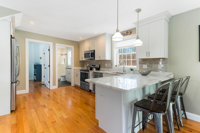 kitchen with tasteful backsplash, a peninsula, a kitchen breakfast bar, stainless steel appliances, and a sink