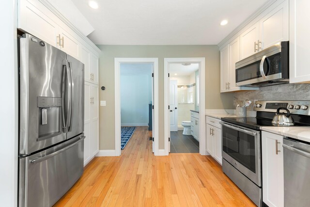 kitchen with baseboards, decorative backsplash, light wood-style flooring, white cabinets, and stainless steel appliances