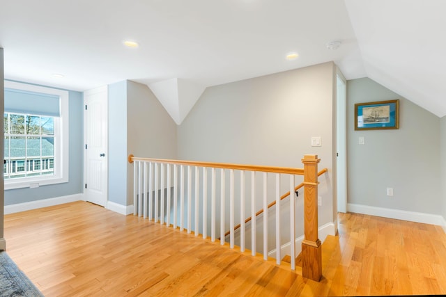 hallway with an upstairs landing, lofted ceiling, baseboards, and wood finished floors