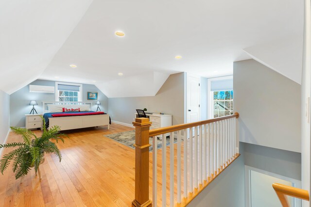 bedroom featuring multiple windows, wood-type flooring, an AC wall unit, and vaulted ceiling