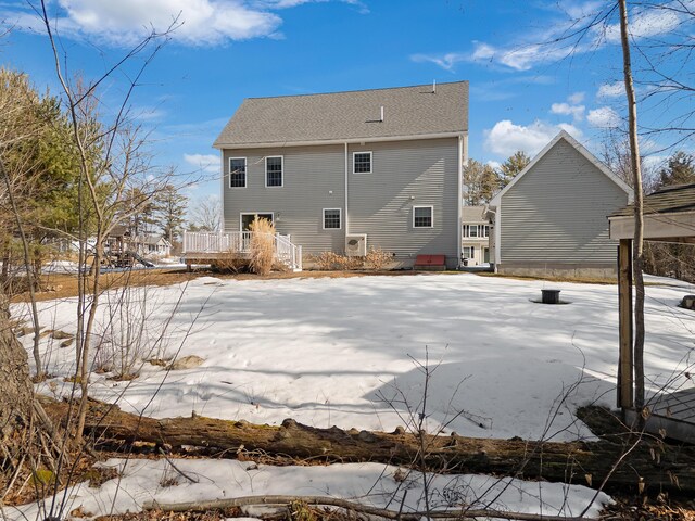 snow covered rear of property with roof with shingles and a deck