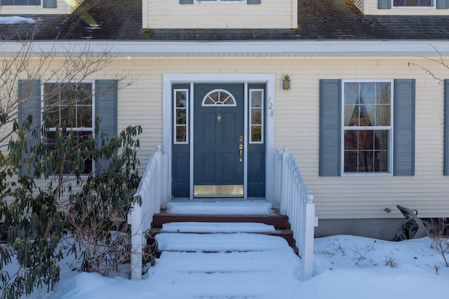 snow covered property entrance with a shingled roof