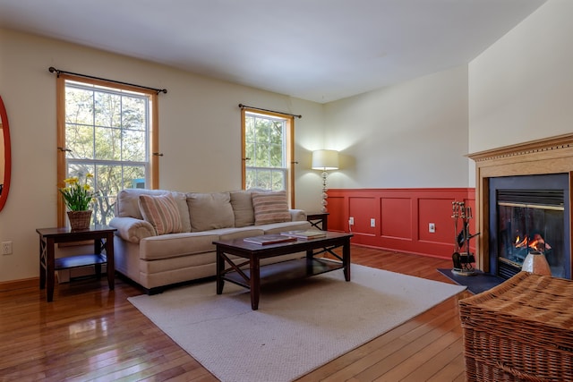 living area with a wainscoted wall, a fireplace with flush hearth, hardwood / wood-style flooring, and a decorative wall