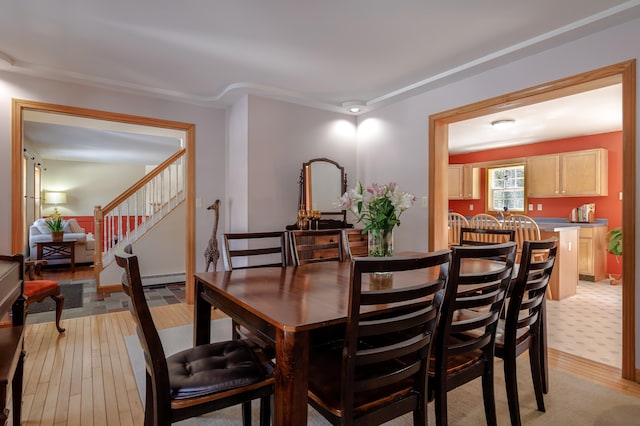 dining area featuring a baseboard radiator, stairway, and light wood-style flooring