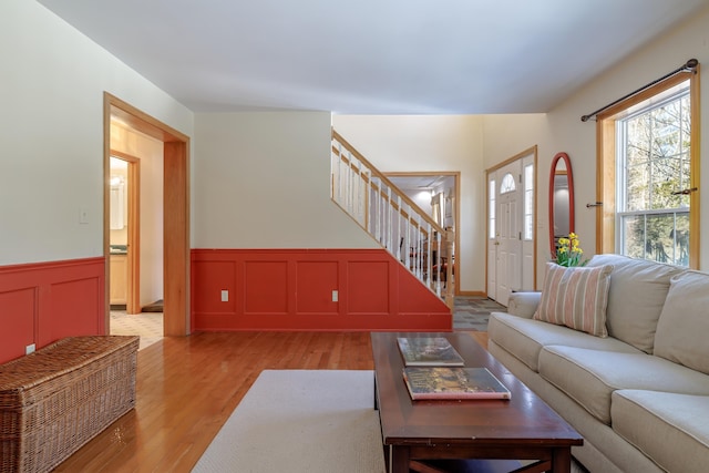 living area with light wood finished floors, stairway, and a wainscoted wall