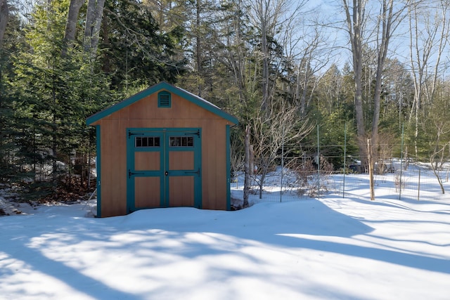 snow covered structure with an outbuilding, a view of trees, and a storage unit