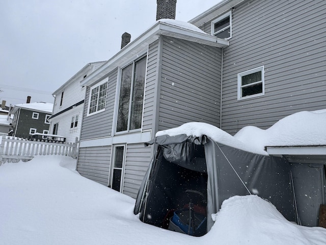 view of snow covered exterior with a chimney and fence